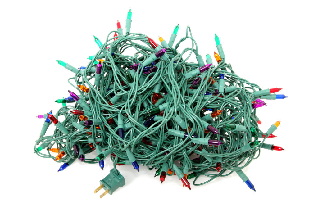 A tangled ball of multicolored Christmas string lights with green wiring on a white background.