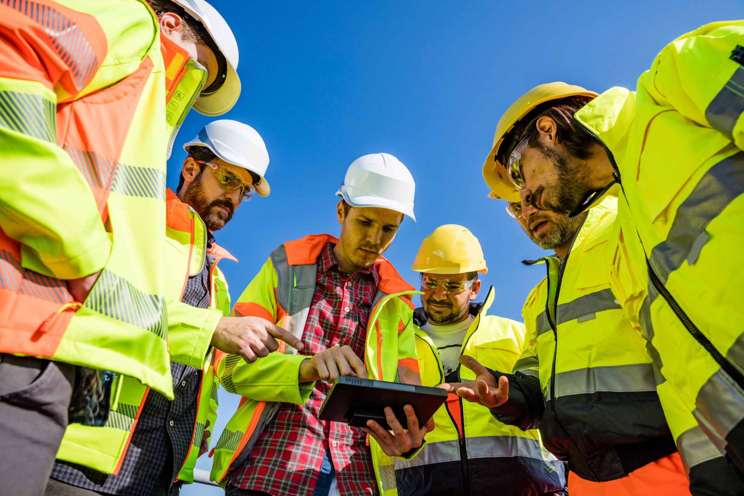 Construction crew gathered around a tablet while collaborating on a jobsite.