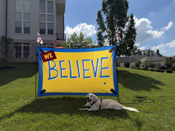 Glenna rests beneath a “We Believe” sign decorated with England flags during the 2026 World Cup in Kansas City.